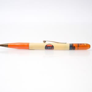 May include: A vintage pen with a cream barrel and orange accents. The pen has a metal clip and a logo with the text "CLUB". The tip is dark brown. The pen is a writing instrument, suitable for everyday use.