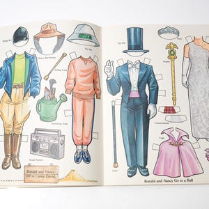 May include: Open book with paper dolls and accessories. The outfits include a riding ensemble, casual wear, and formal attire. The text reads "Ronald and Nancy Off to Camp David" and "Ronald and Nancy Go to a Ball."