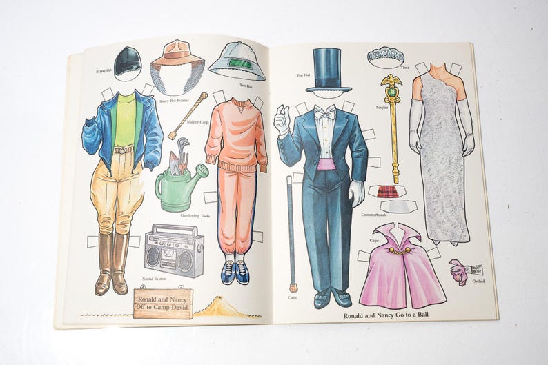 May include: Open book with paper dolls and accessories. The outfits include a riding ensemble, casual wear, and formal attire. The text reads "Ronald and Nancy Off to Camp David" and "Ronald and Nancy Go to a Ball."