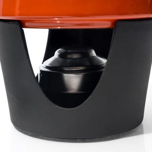 May include: Close-up of a fondue pot with a black metal stand and a bright orange pot. The stand has a curved design with an opening for the fuel source. The pot is round and sits securely on the stand.