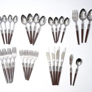 May include: A collection of stainless steel cutlery with dark brown wooden handles. The set includes spoons, forks, knives, and a butter knife. The cutlery has a decorative design on the handle.