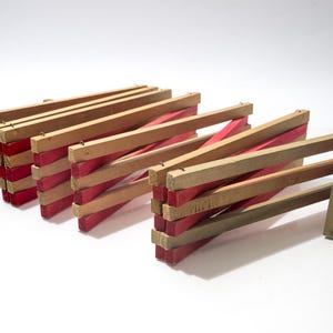 May include: Wooden folding fence sections with alternating red and natural wood slats. The sections are connected with small metal hinges. The fence is designed to be expandable and collapsible, ideal for decorative purposes.
