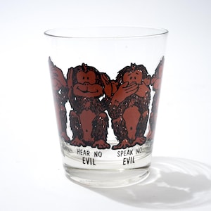 May include: Clear glass with a brown cartoon illustration of three monkeys. The monkeys cover their ears, eyes, and mouth. The text "HEAR NO EVIL" and "SPEAK NO EVIL" are printed below the monkeys. A fun, novelty drinking glass.