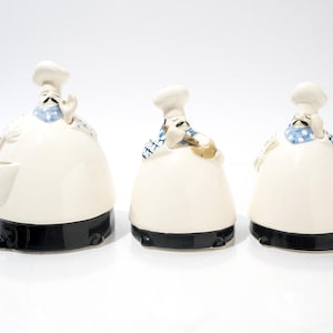May include: Three ceramic chef figurines. Each figurine is white with a black base, a chef's hat, and a blue and white checkered neckerchief. One chef has a pocket, and all have a mustache.