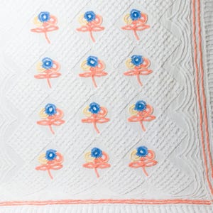 May include: White quilted blanket with a repeating pattern of embroidered flowers in shades of pink, blue, and yellow.