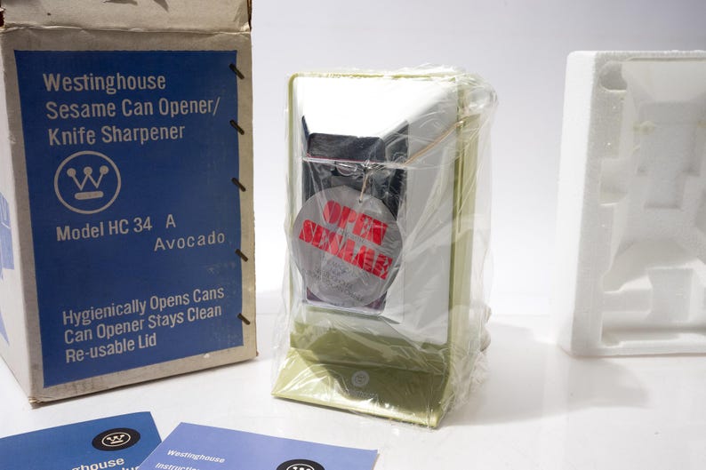 May include: A vintage Westinghouse Sesame Can Opener/Knife Sharpener, model HC 34 A, in its original box. The box is blue and white with product information. The can opener is avocado-colored and wrapped in plastic. A tag reads "OPEN SUMMER".
