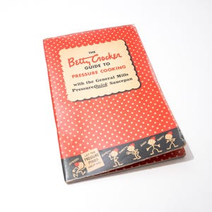 May include: A vintage cookbook titled "The Betty Crocker Guide to Pressure Cooking" with a red cover and white polka dots. The book features a cream-coloured label with text and illustrations of cartoon characters.
