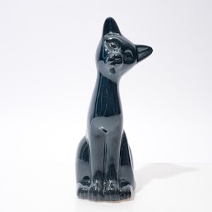 May include: A glossy, dark teal ceramic cat figurine in a seated position with its head tilted. The cat has a sleek, modern design with pointed ears and detailed paws. The figurine is approximately 10 inches tall.