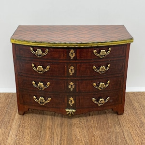 May include: A four-drawer wooden chest of drawers with a marquetry top and brass hardware. The chest has a curved front and is painted a dark brown color.