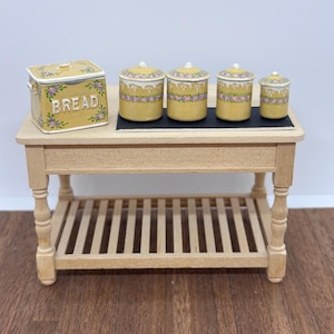 May include: A miniature wooden kitchen island with a slatted lower shelf, topped with a yellow ceramic bread box labeled BREAD and four matching yellow ceramic canisters of varying sizes, all decorated with a floral pattern of pink and purple flowers.