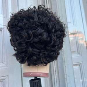 May include: A black curly wig on a mannequin head. The wig is styled in a short, curly bob.