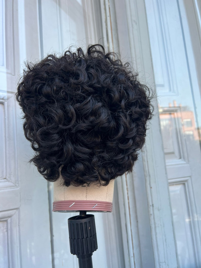 May include: A black curly wig on a mannequin head. The wig is styled in a short, curly bob.