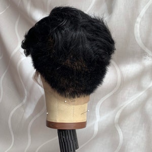 May include: Black wig on a mannequin head with a brown base and a black stand. The wig is styled in a short, textured look.