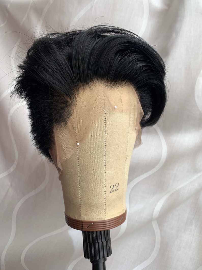 May include: A black wig with a lace front on a wig stand. The wig is styled in a short, textured look. The wig stand is labeled with the number 22.
