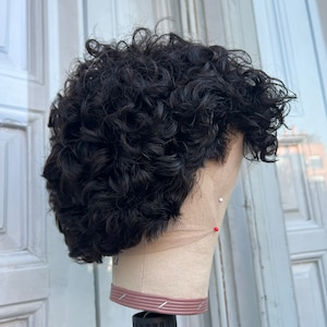 May include: A black curly wig on a mannequin head. The wig is styled in a short, textured look.