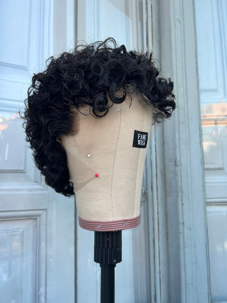 May include: A black curly wig on a mannequin head with a label that says "FAME WIGS".