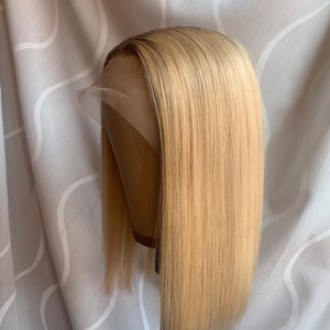 May include: A blonde human hair wig with a straight style and a lace front. The wig is on a mannequin head.