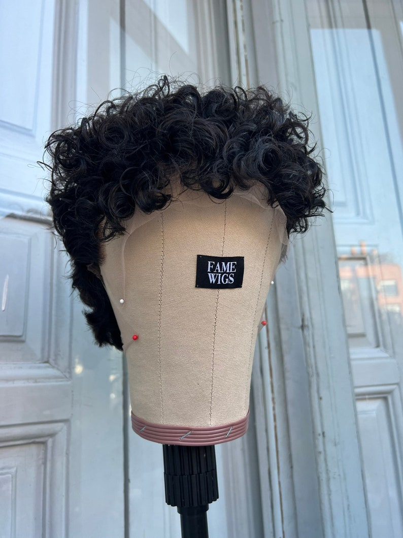 May include: A black curly wig on a mannequin head with a label that says "FAME WIGS".