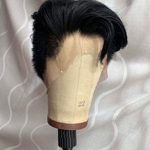 May include: Black men's wig with a short, styled haircut. The wig is on a mannequin head with a brown base and the number 22 printed on it.