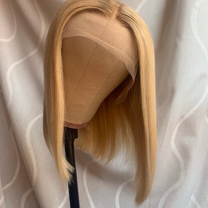 May include: A blonde bob wig on a wig stand. The wig is styled in a straight bob with blunt ends.