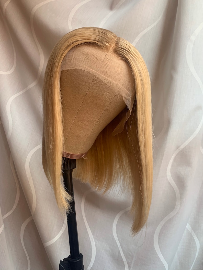 May include: A blonde bob wig on a wig stand. The wig is styled in a straight bob with blunt ends.