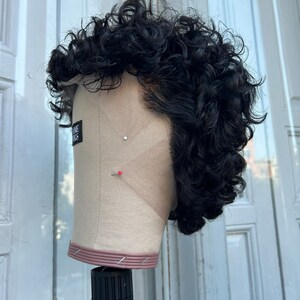 May include: A black curly wig on a mannequin head. The wig is styled in a short, textured look. The mannequin head is on a black stand.