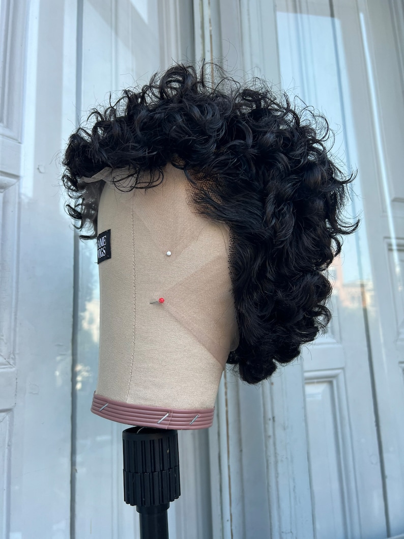 May include: A black curly wig on a mannequin head. The wig is styled in a short, textured look. The mannequin head is on a black stand.