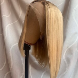 May include: A blonde bob wig with a straight style. The wig is on a wig stand and has a light brown colour.