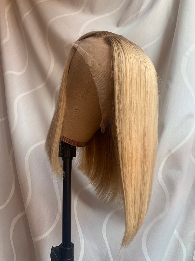 May include: A blonde bob wig with a straight style. The wig is on a wig stand and has a light brown colour.