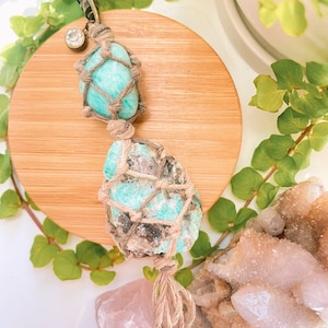 May include: A green and brown crystal keychain with a macrame wrap. The keychain is made with natural materials and has a rustic look.