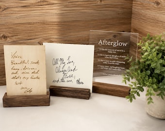 May include: Three rectangular displays with dark wood bases. One is a light wood plaque with handwritten text, one is a white card with black cursive script, and one is a clear acrylic sign with the printed poem Afterglow by Helen Lowrie Marshall.