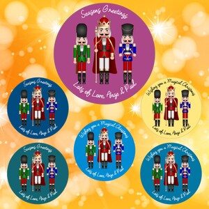 以下が含まれることがあります： ナッツクラッカーをテーマにした丸いクリスマスギフトタグが6つ。各タグには、金色のアクセントが施された赤、緑、青のナッツクラッカーが3つ描かれています。タグには、「Seasons Greetings」、「Wishing you a Magical Christmas」、「Lots of Love, Ange & Paul」など、さまざまな挨拶が書かれています。