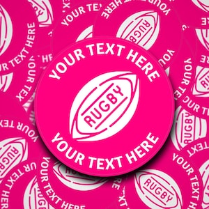 以下が含まれることがあります： ピンクの丸い床用ステッカーに、白いラグビーボールのグラフィックと「YOUR TEXT HERE」のテキストが書かれています。