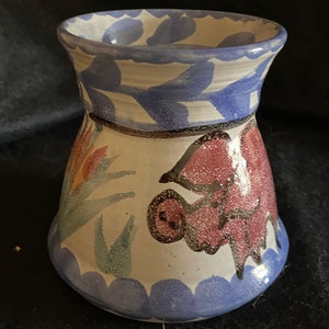 Könnte beinhalten: Eine weiße Keramikvase mit einem blauen und weißen Blumenmuster. Die Vase hat eine breite Öffnung und einen schmalen Boden. Die Vase ist mit einem rosa und grünen Blumendesign verziert.