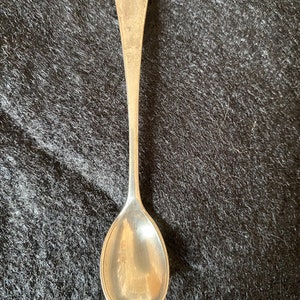 Puede incluir: Una cucharadita de plata con un cuenco redondeado y un mango largo y delgado.