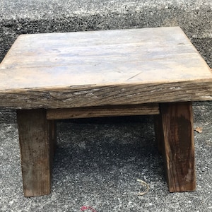 May include: A rustic wooden stool with a rectangular top and four legs. The stool is made of weathered wood with a natural finish.