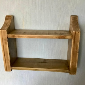 May include: A two-tiered wooden shelf with a natural wood finish. The shelf is mounted to a wall and has a simple, rustic design.