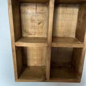May include: A wooden shelf unit with four square compartments. The shelf is made of natural wood with a light brown finish.