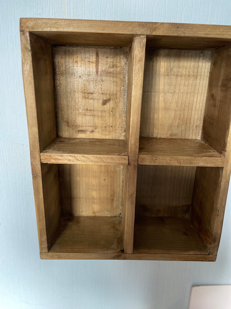 May include: A wooden shelf unit with four square compartments. The shelf is made of natural wood with a light brown finish.