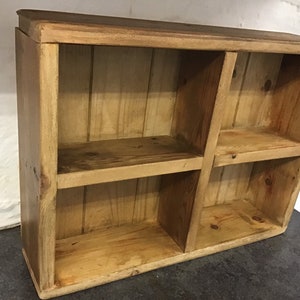 May include: A rustic wooden shelf unit with four open compartments. The shelf is made of natural wood with a light brown finish.