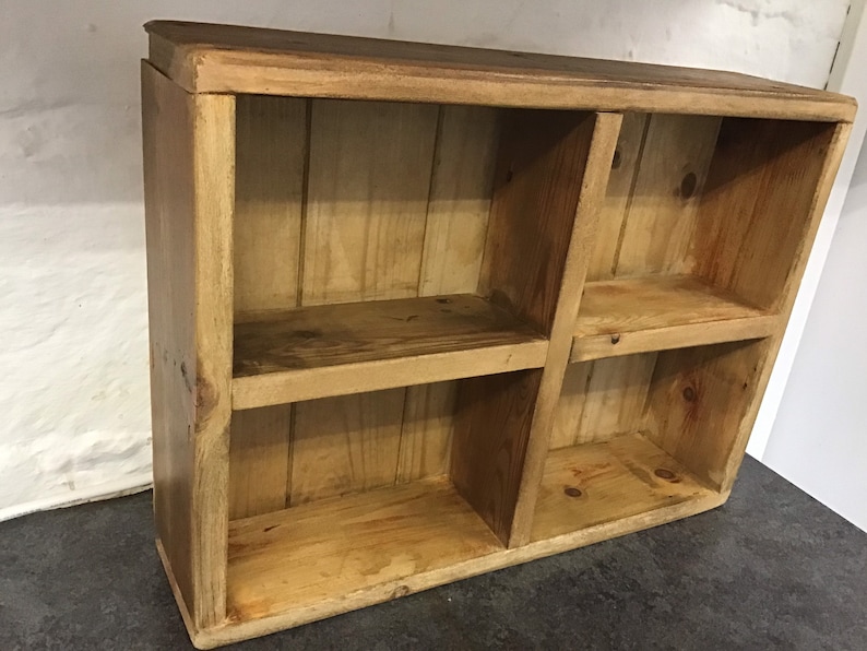 May include: A rustic wooden shelf unit with four open compartments. The shelf is made of natural wood with a light brown finish.