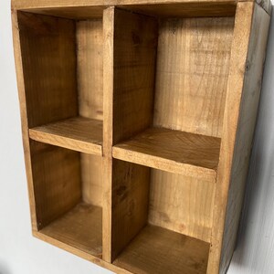 May include: A wooden shelf unit with four square compartments. The shelf is made of natural wood with a light brown stain.