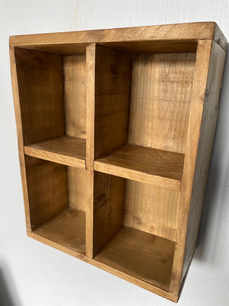 May include: A wooden shelf unit with four square compartments. The shelf is made of natural wood with a light brown stain.
