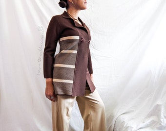 May include: A brown blazer with a cream-coloured striped panel on the front. The blazer has a double-breasted design and is paired with beige trousers. The outfit is set against a white backdrop.