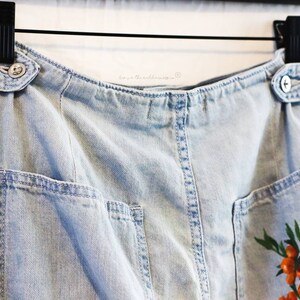 May include: Light blue denim skirt with a belt, two pockets, and a floral print with orange berries.