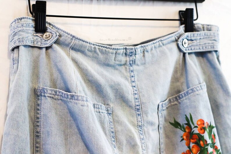 May include: Light blue denim skirt with a belt, two pockets, and a floral print with orange berries.