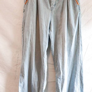 May include: Light blue denim jeans with orange stitching detail on the pockets and seams. The jeans have a high waist and a wide leg.