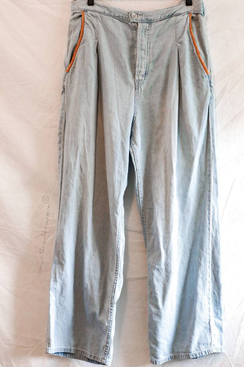May include: Light blue denim jeans with orange stitching detail on the pockets and seams. The jeans have a high waist and a wide leg.