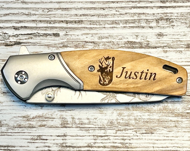 Op de afbeelding: Een gepersonaliseerd zakmes met een houten handvat. Het handvat is voorzien van een lasergegraveerd beeld van een hert met een vislood en de naam "Justin".