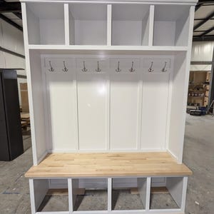 May include: White wooden entryway bench with a built-in cubby storage system and a top shelf. The bench has a light wood top and a white painted finish.
